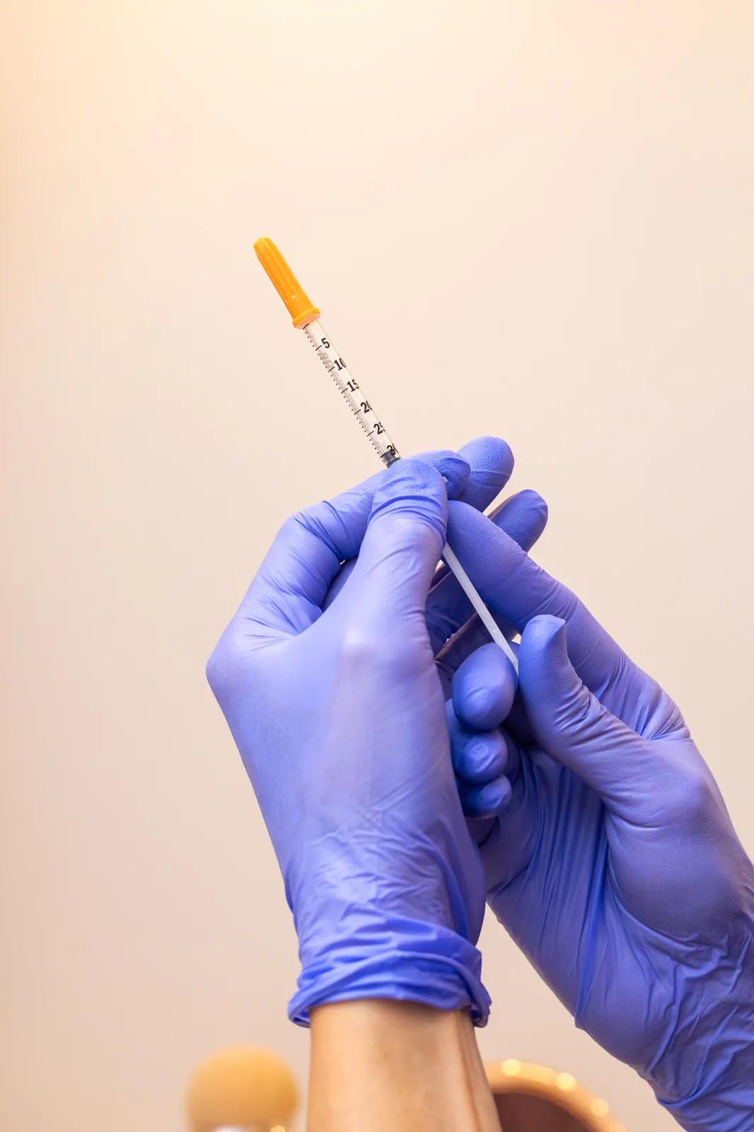 Manos con guantes sosteniendo una jeringa de aguja fina antes de una aplicación de toxina botulínica